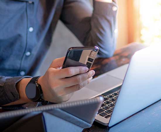 Man holding phone in front of laptop.