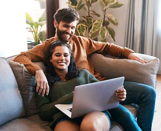 Couple using laptop on couch at home.
