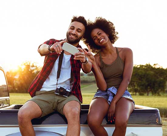 Couple sitting on truck taking selfie.